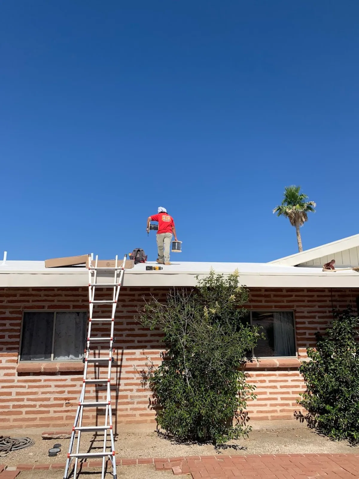 PRC technician on the roof of a brick desert home with a ladder in place under a clear Tucson sky.