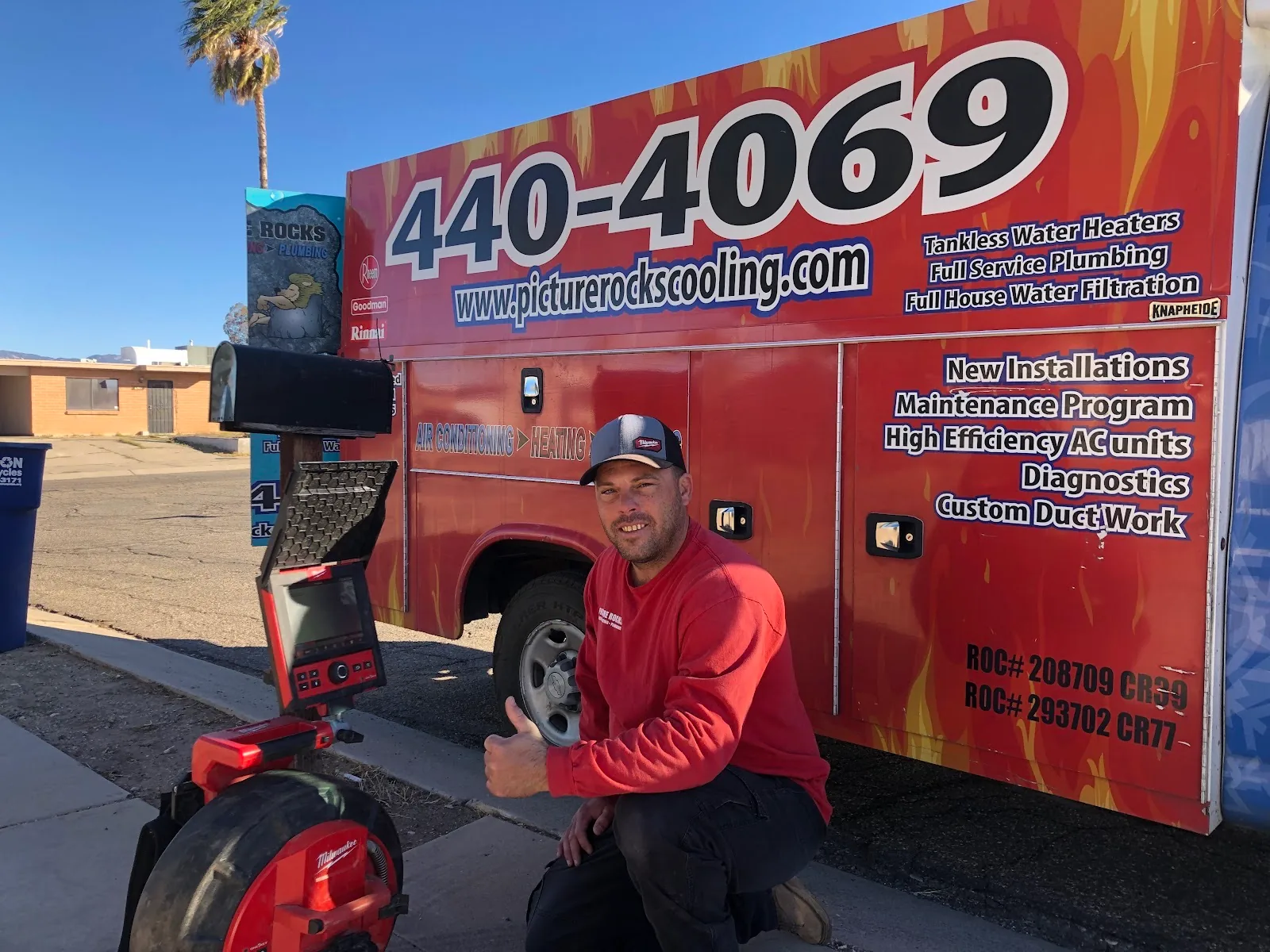 PRC technician in a red polo standing at a red-wrapped service truck under a blue desert sky.