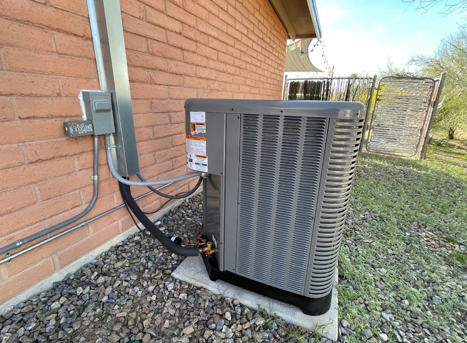 Outdoor condenser unit installed beside a brick home with desert landscaping