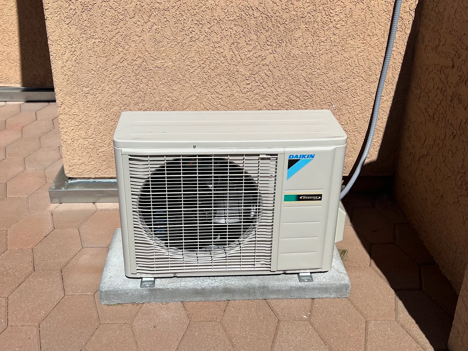 Ductless mini-split condenser unit installed on a pad against a stucco exterior wall