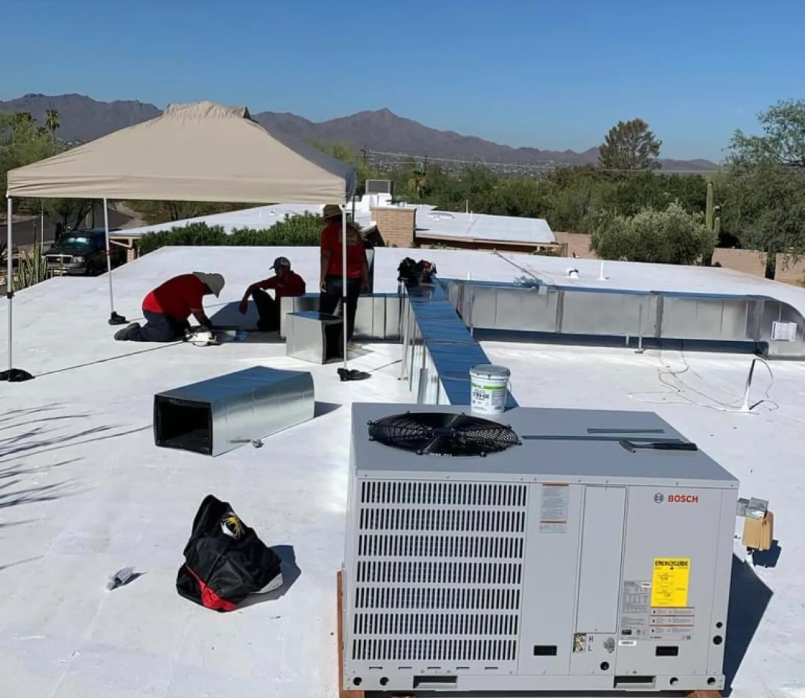 Installation crew setting a rooftop air conditioning unit under a shade canopy with Tucson mountains in the background