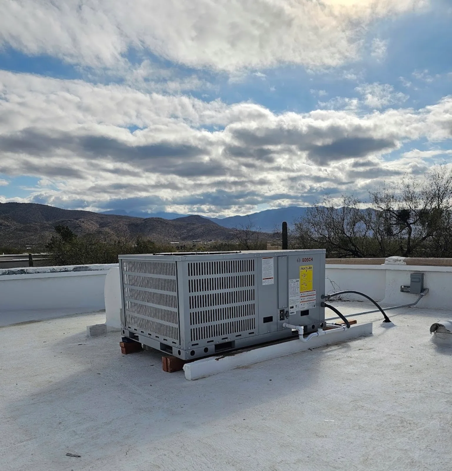 Rooftop air conditioning package unit installed against a backdrop of Tucson mountains and clouds