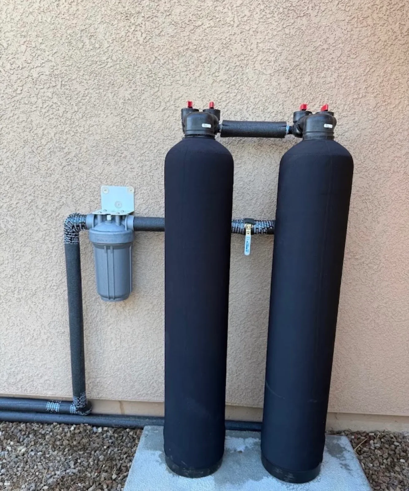 Twin water softener and filtration tanks installed with clean copper piping against a stucco wall.